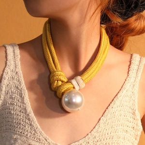 Artistic yellow braided rope necklace featuring a large pearl pendant worn by a model