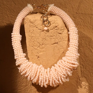 Macro shot of peach-toned beaded braided necklace draped over natural earthy rock texture