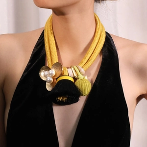 Détail d'un collier en corde jaune avec pompon en soie et pendentif fleur en perles