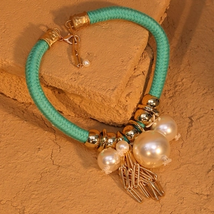Dettaglio della collana bohémien in corda verde intrecciata con perle e nappe dorate