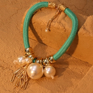 Dettaglio della collana in corda verde con grandi perle e nappe in metallo dorato