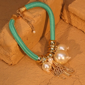 Dettaglio della collana in corda intrecciata verde con metallo dorato e nappe di perle