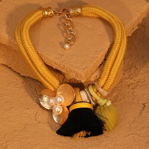 Détail du collier tressé jaune avec fleur dorée, perles blanches et gland noir fin