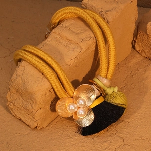 Détail du collier en corde tressée avec fleur dorée, perles et pompon en soie noire
