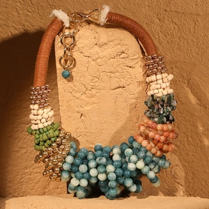 Détail d'un collier bohème avec des perles bleues, vertes et dorées sur support brut