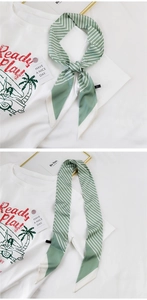 Detail eines schmalen, grün gestreiften Seidenschals auf einem weißen Grafik-T-Shirt