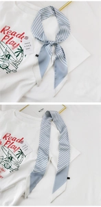 Detail eines blau-weiß gestreiften Seidenschals, gebunden als Schleife auf weißem T-Shirt