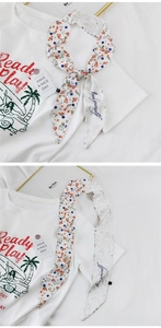 Detail eines geblümten schmalen Schals und eines weißen Grafik-T-Shirt-Sets auf Stoffhintergrund