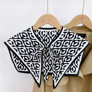Detail of a black and white geometric shawl collar with letter C ring and bow tie closure