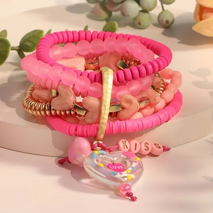 Bracelets bohèmes superposés avec perles roses, tubes dorés et breloques cœur