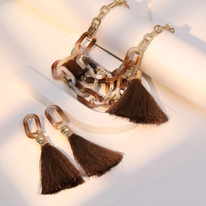 Detail of amber acrylic chain necklace and brown tassel earrings on white pedestal