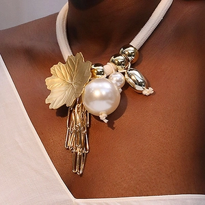 Detail of bohemian maple leaf pendant with pearl and tassel on braided rope necklace