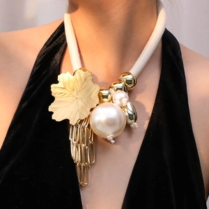 Detail of bohemian necklace with large gold leaf, pearl and tassels on a black dress