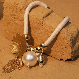 Detailed view of bohemian leaf charm with pearl and golden chain tassels on woven rope