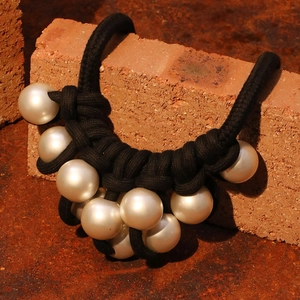 Exaggerated large pearl pendant necklace with black woven rope on a rustic background