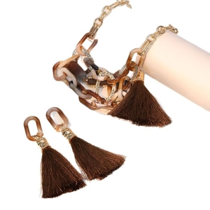Bohemian jewelry set with amber resin links and dark brown silk tassels on white pedestals