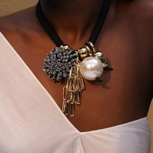 Detail of flower necklace with faux pearl, gold chains, and black woven rope on model