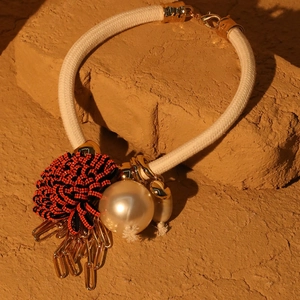 Detailed close-up of beaded flower necklace with large pearl and golden fringe on rustic rock