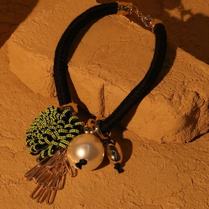 Detail of floral faux pearl necklace with black cord and dangling gold metal chain tassels