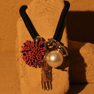 Detailed close-up of a floral necklace featuring red woven ball, pearl, and gold tassel