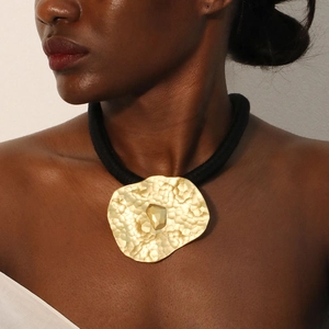 Detail of chunky gold hammered pendant on black waxed cord necklace worn by model