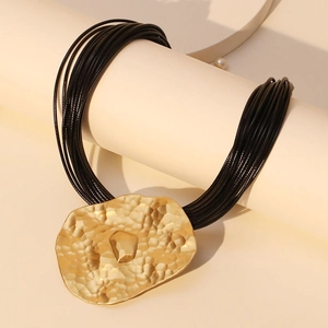 Multi-strand wax cord necklace with irregular hammered gold pendant in warm studio lighting