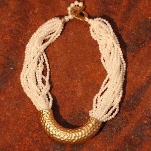 Multi-layer pearl necklace with golden curved tube and T-bar clasp on textured background