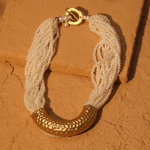 Detailed close-up of multi-layer pearl necklace with textured gold U-shaped metal pendant
