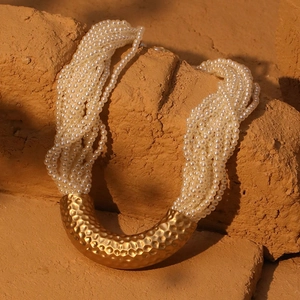 Macro shot of gold hammered U-shape pendant on multi-layered white pearl necklace