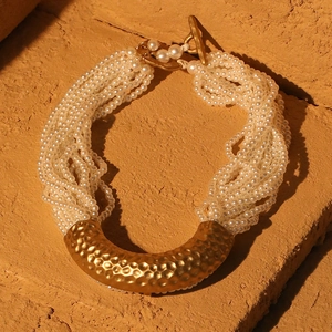 Detail of multi-strand pearl necklace featuring a hammered gold U-shaped metal pendant