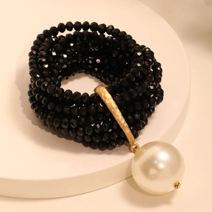 Macro detail of multi-layer black beaded bracelet featuring a large faux pearl pendant