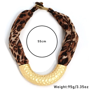 Close-up of matte gold U-shaped pendant with hammered texture and leopard print fabric strap