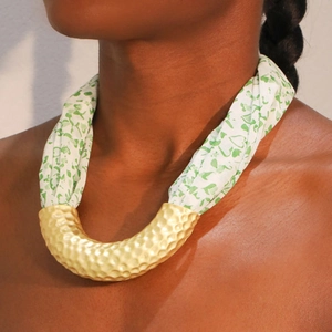 Close-up of a U-shaped gold hammered metal tube necklace with green floral fabric straps