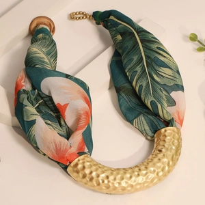 Macro view of tropical leaf print fabric and hammered gold metal U-shaped pendant