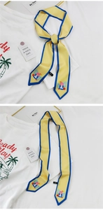 Détail d'un foulard en soie jaune avec bordure bleue et illustration noué sur un t-shirt