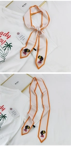 Détail d'un foulard twilly beige avec bords orange et imprimé portrait ethnique