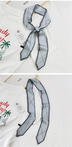 Détail d'un foulard étroit bleu-gris à motif quadrillé noué en forme de nœud chic