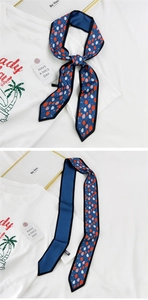 Détail d'un long foulard à motif fraises noué en nœud sur un t-shirt blanc classique