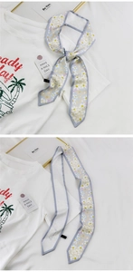 Détail d'un foulard étroit en soie à motif marguerites avec citation et bordure bleue