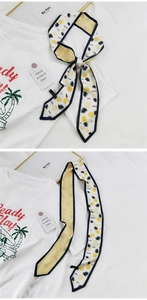 Détail d'un foulard twilly blanc étroit avec imprimé d'ananas jaunes et bordures noires