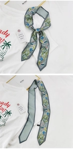 Détail d'un foulard twilly en soie bleu clair à motif floral, porté comme accessoire sur un t-shirt