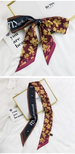 Détail d'un foulard en soie bordeaux à fleurs noué en boucle et posé à plat sur tissu