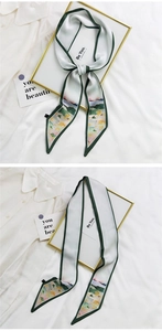 Gros plan sur un foulard étroit en soie crème avec bordure verte et imprimé artistique