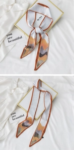Détail d'un foulard en soie à motif abstrait orange et blanc élégamment noué sur un tissu