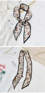 Détail d'un foulard étroit en soie à fleurs oranges avec bordure noire fine