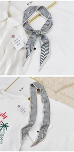 Détail d'un foulard étroit en soie avec motifs chevrons noirs sur fond beige clair