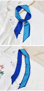 Détail d'un foulard étroit en soie bicolore bleu noué sur un col de chemise blanc