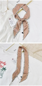 Détail d'un élégant foulard twilly en satin champagne avec imprimé de lettres