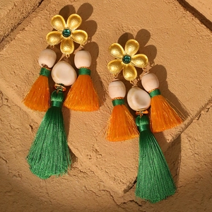 Böhmische Blumenohrringe mit orangefarbenen und grünen Fransen auf einer Steinoberfläche