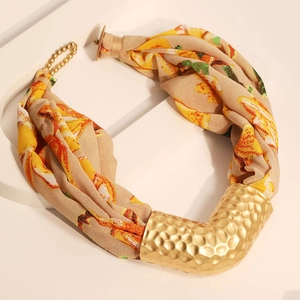 Macro detail of V-shaped hammered gold pendant with orange floral fabric bohemian choker